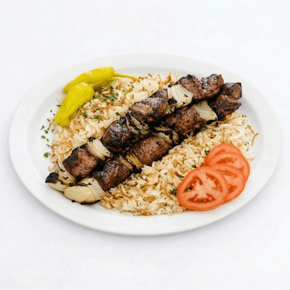 Two skewers of grilled meat and onions on a bed of rice, with sliced tomatoes and peppers.
