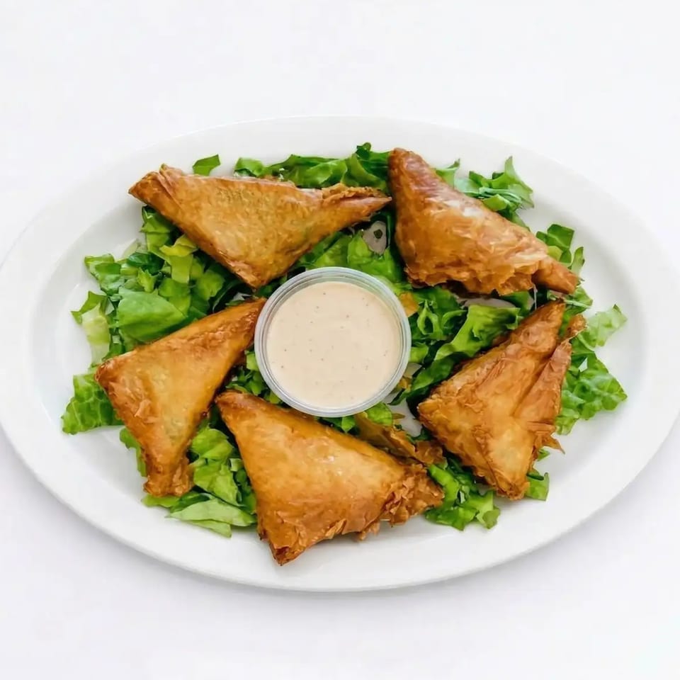 Five golden-brown triangular pastries, possibly samosas or spanakopita, arranged on a bed of fresh green lettuce with a small cup of dipping sauce in the center.